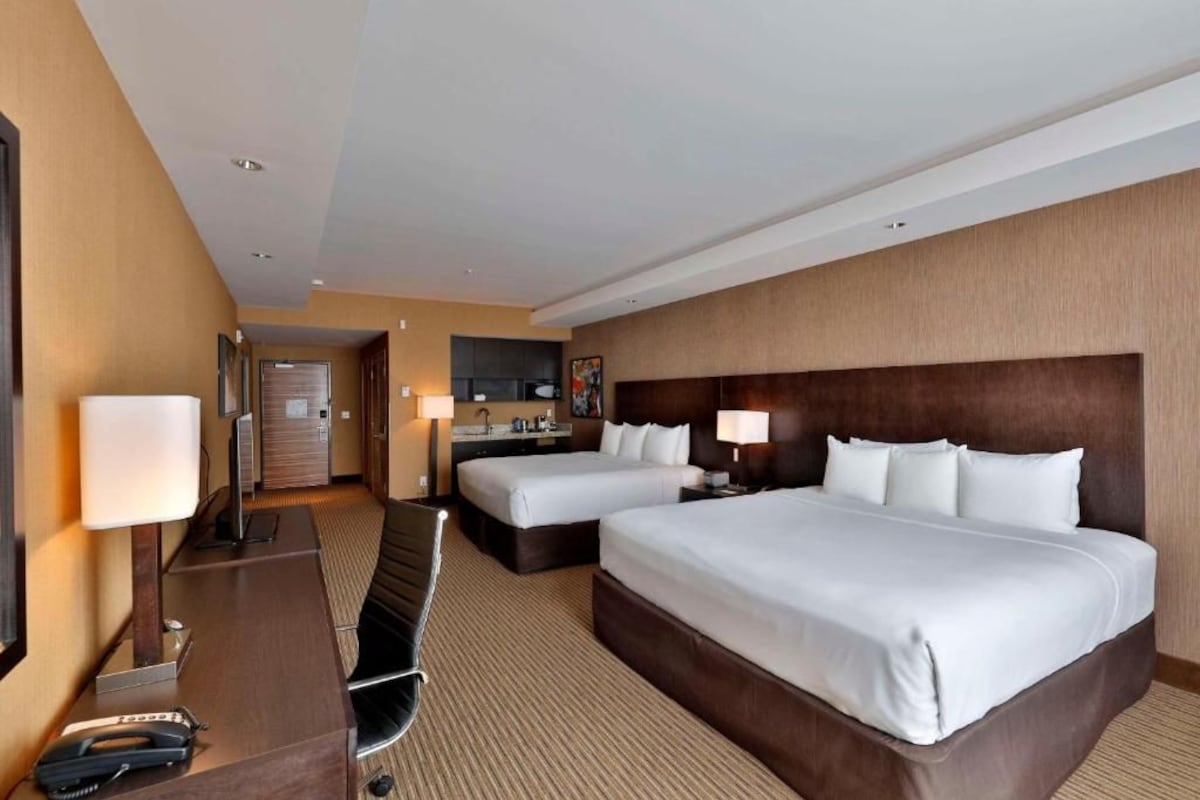 A hotel room with two beds, a desk, a chair, a desk lamp, a telephone, and a television.