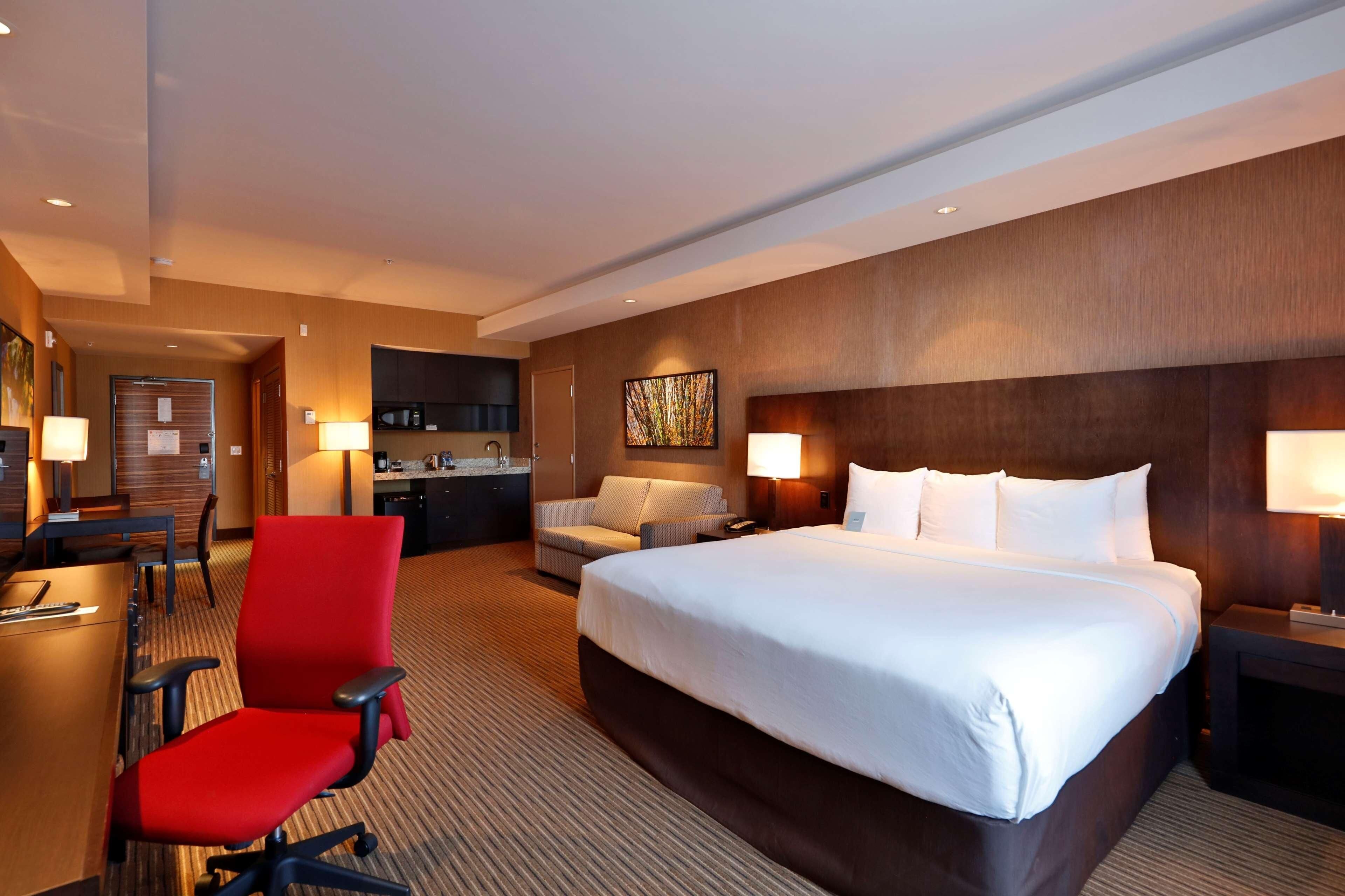 Habitación de hotel con una cama grande, un escritorio con una silla, un sofá y una zona de kitchenette.