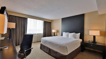 Habitación de hotel con una cama grande, un escritorio con silla, dos lámparas de noche y una ventana con cortinas.