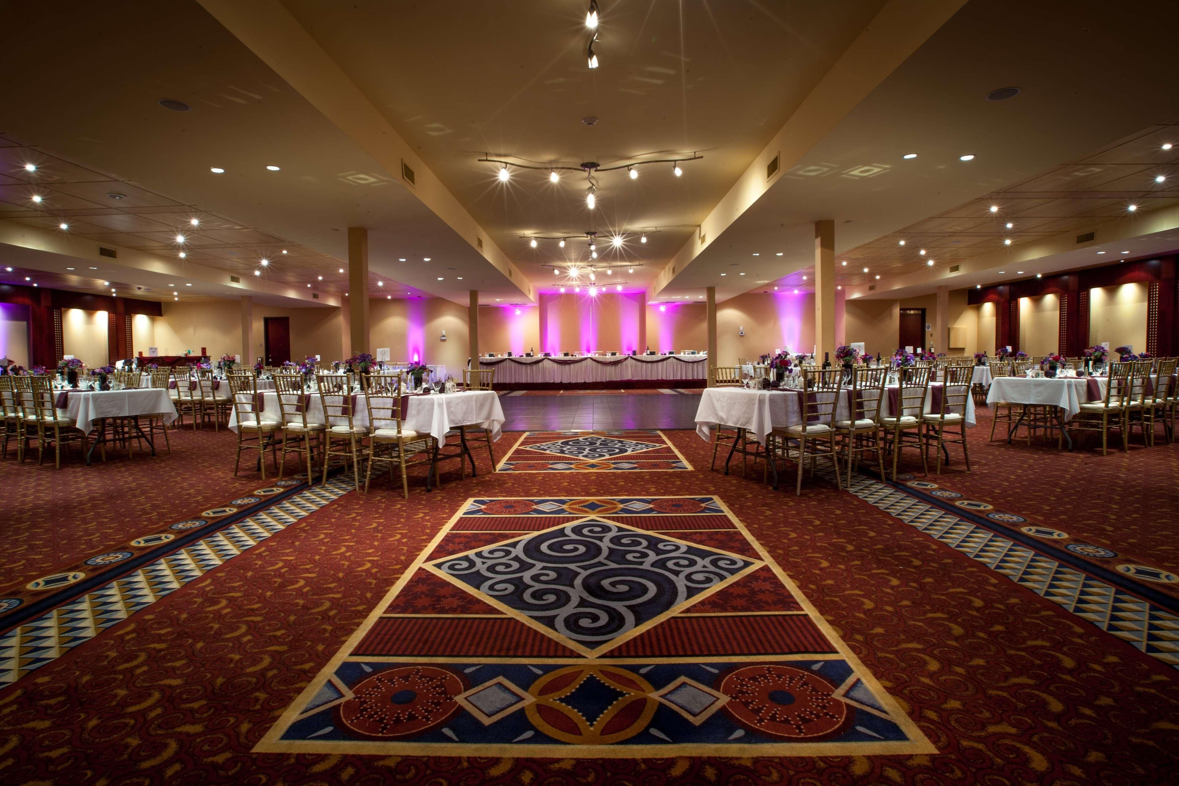 Un salón de banquetes con mesas dispuestas en filas, una alfombra estampada y un escenario al frente.