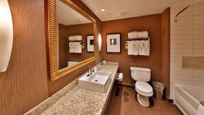 A hotel bathroom with a large mirror, a sink, a toilet, and a bathtub. - Edmonton Hotel & Convention Center (Edmonton)
