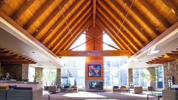 A spacious lobby with a high wooden ceiling, large windows, and a central fireplace.