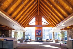 A spacious lobby with a high wooden ceiling, large windows, and a central fireplace. - Edmonton Hotel & Convention Center (Edmonton)