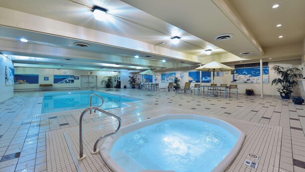 An indoor swimming pool with a hot tub, tiled flooring, and seating areas. - Edmonton Hotel & Convention Center (Edmonton)