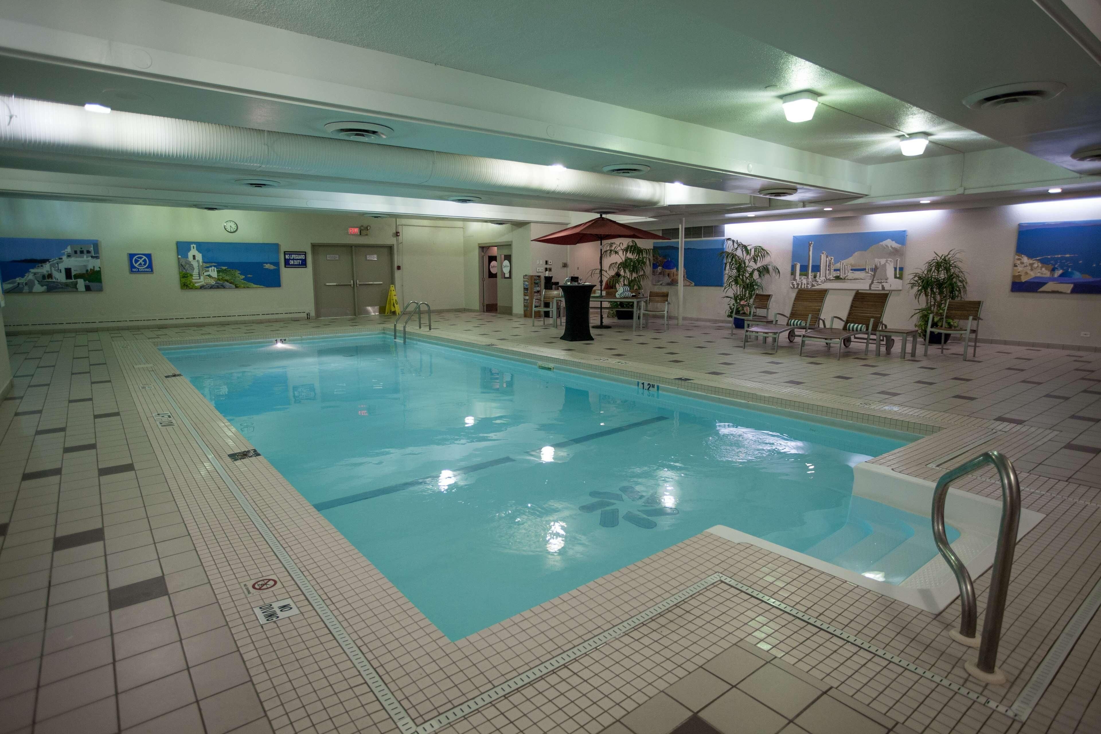 An indoor swimming pool with tiled floors, a lifeguard chair, and a seating area with tables and chairs.