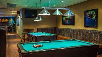 A pool table with a green felt surface, a bar area with stools, and a seating area with a patterned bench.