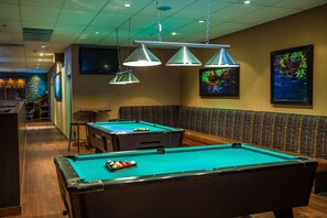 A pool table with a green felt surface, a bar area with stools, and a seating area with a patterned bench. - Edmonton Hotel & Convention Center (Edmonton)