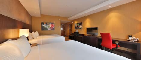 A hotel room with two beds, a desk with a TV, and a red chair.