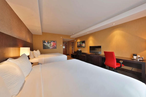 Quarto de hotel com duas camas, uma escrivaninha com televisão e uma cadeira vermelha.