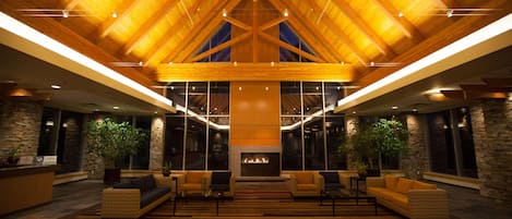 A lobby with a high wooden ceiling, a fireplace, and seating areas with plants.