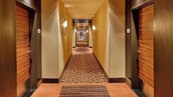 Un corridoio d'hotel con porte in legno, una moquette fantasia e illuminazione a soffitto.
