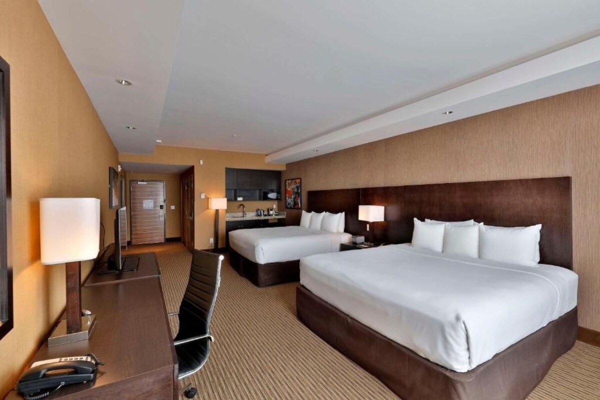 Une chambre d’hôtel avec deux lits, un bureau, une chaise, une lampe de bureau, un téléphone et une télévision.