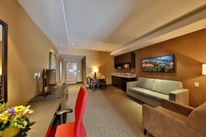 Habitación de hotel con sofá, televisión, zona de comedor y cocina.