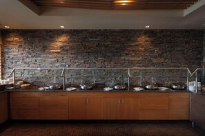 A buffet setup with a stone wall backdrop, wooden cabinets, and a patterned floor. - Edmonton Hotel & Convention Center (Edmonton)