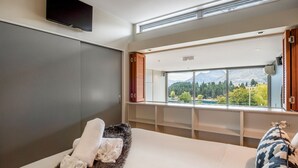 A bedroom with a large window, a flat-screen TV, and a fur rug. - Pounamu Terrace | Central · Lakeview · Fireplace (Queenstown)
