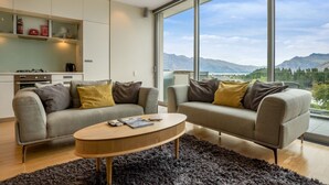 A modern living room with two sofas, a coffee table, and a view of mountains through large windows. - Pounamu Terrace | Central · Lakeview · Fireplace (Queenstown)