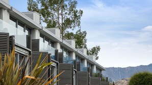 A modern multi-story building with balconies, large windows, and a mountainous backdrop. - Pounamu Terrace | Central · Lakeview · Fireplace (Queenstown)
