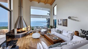 A modern living room with a fireplace, white furniture, and a large window overlooking a scenic view. - Villa Vollard  | 5 Bedrooms with Private Pool Jacuzzi and Panoramic Sea View (Heraklion)