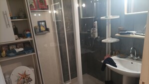 Kylpyhuone, jossa on wc, suihku, pesuallas ja hyllyjä, joilla on hygieniatuotteita.