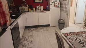 Pieni, käytännöllinen keittiö, jossa on valkoiset kaapit, jääkaappi, kello ja roskakori.
