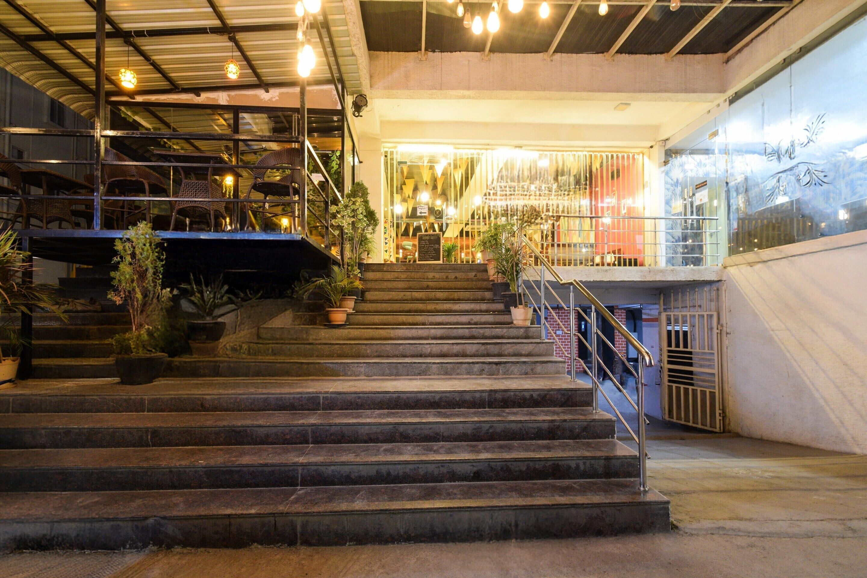 A staircase leading to a restaurant with outdoor seating, potted plants, and a metal railing.
