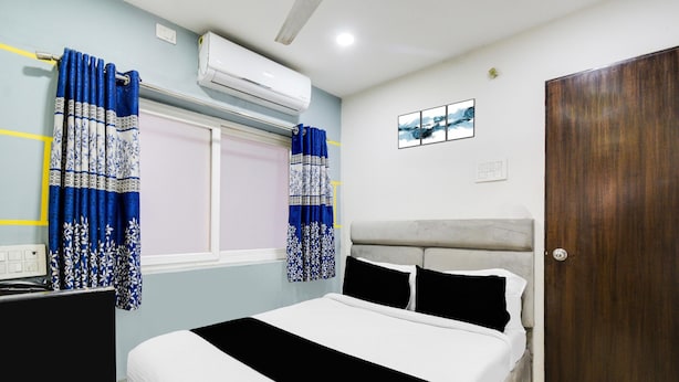 A bedroom with a bed, curtains, an air conditioner, a wall-mounted picture, and a door. - Townhouse Hitec City Metro Station (Hyderabad)