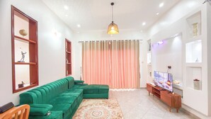 Una sala de estar con un sofá seccional verde, un tapete estampado, un televisor y una lámpara decorativa en el techo.