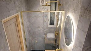 Een badkamer met een marmeren wand, een houten wastafelmeubel, een douchecabine van glas en een toilet.