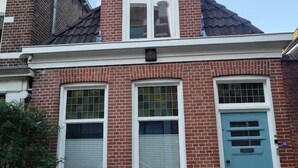 Een tweelaags bakstenen gebouw met een blauwe deur, ramen met witte kozijnen en een klein voortuintje.