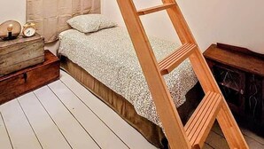 Een slaapkamer in loftstijl met een houten trap, een bed met beddengoed met een patroon, een nachtkastje en een dressoir.
