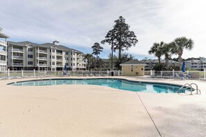 Une piscine entourée d’une clôture blanche, elle-même bordée d’immeubles à plusieurs étages dotés de balcons.