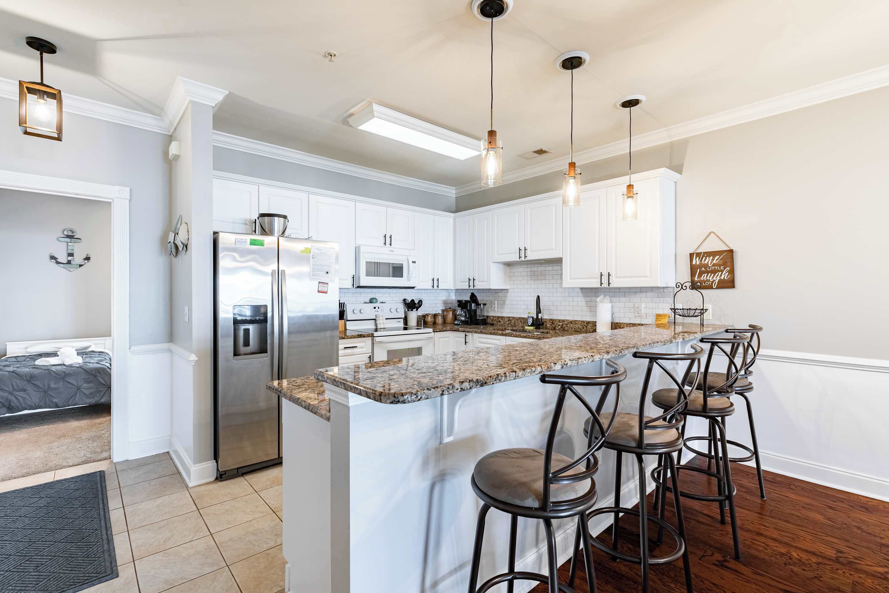 A modern kitchen with white cabinets, a large island with bar stools, stainless steel appliances, and pendant lighting.