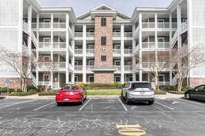 Un immeuble d’habitation à plusieurs étages, doté d’une tour centrale en briques, de balcons et d’un parking pouvant accueillir deux voitures.