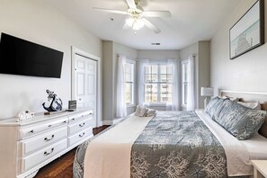 Ein Schlafzimmer mit einem Bett, einem Schminktisch, einem Deckenventilator und einem Fenster mit Vorhängen.
