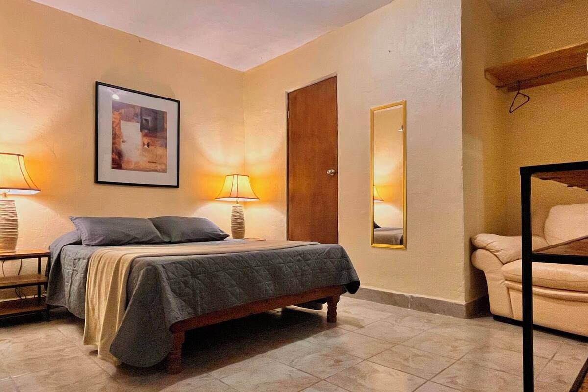 A bedroom with a bed, two bedside lamps, a door, a mirror, and a chair.