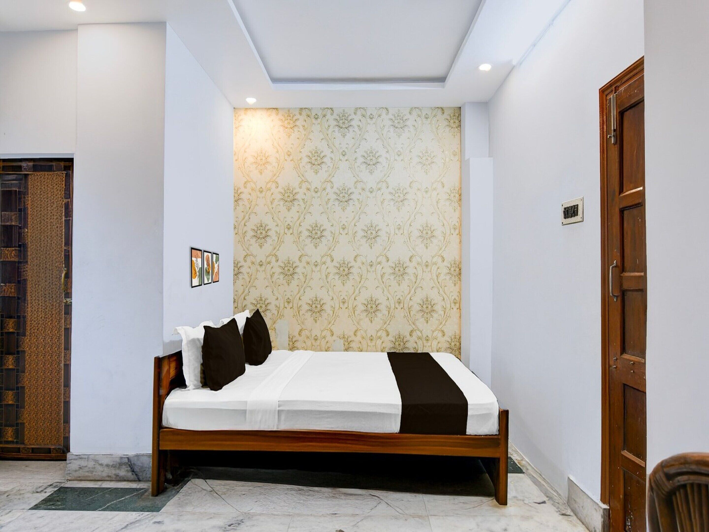 A bedroom with a bed, a patterned wallpaper, a wooden door, and a small picture on the wall.