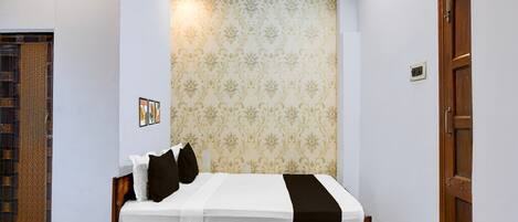 A bedroom with a bed, a patterned wallpaper, a wooden door, and a small picture on the wall.
