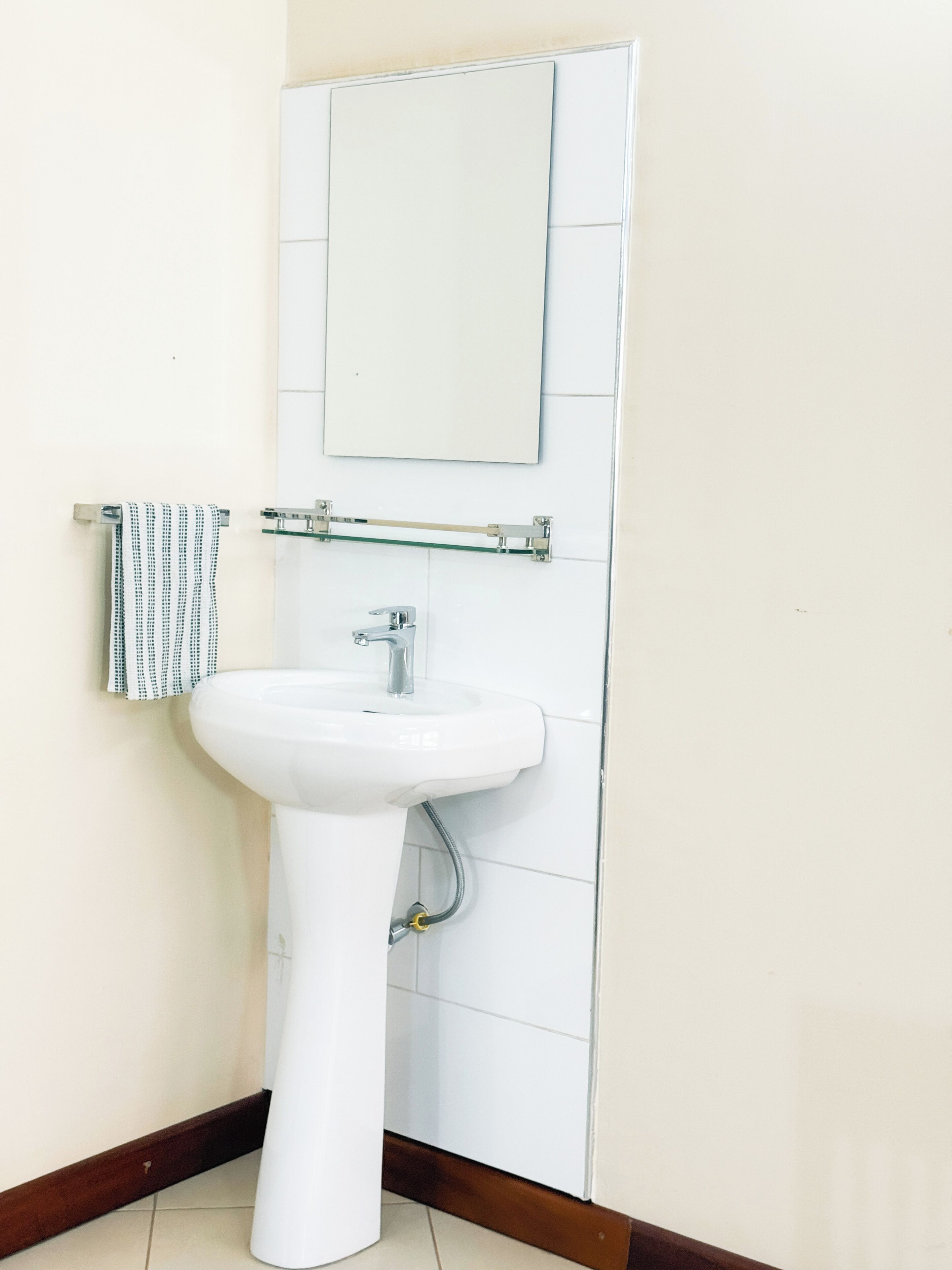Un baño con lavamanos pedestal blanco, un perchero con una toalla estampada, y un espejo sobre el lavamanos.