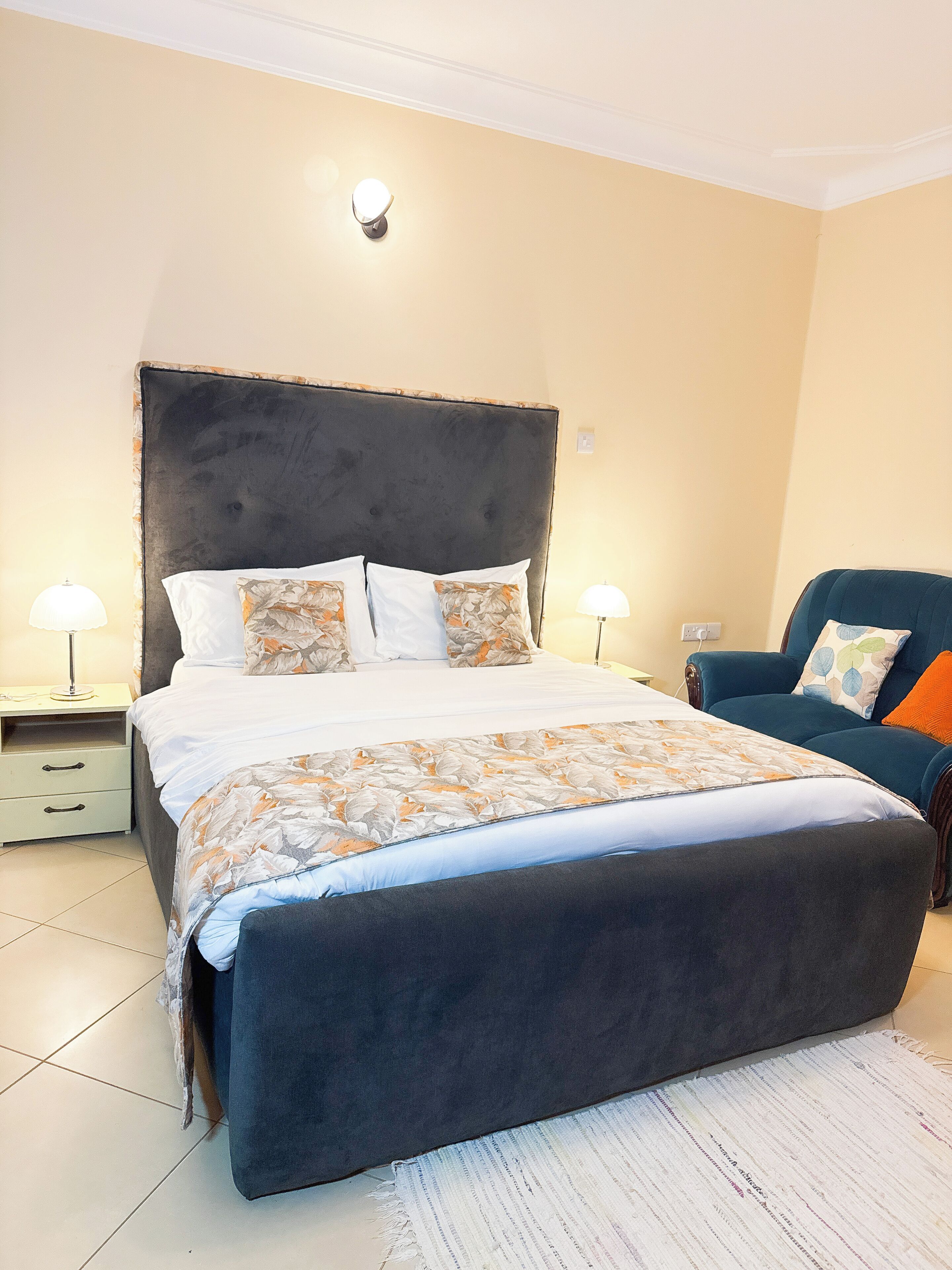 A bedroom with a large bed, two bedside tables, a chair, and a wall-mounted light.