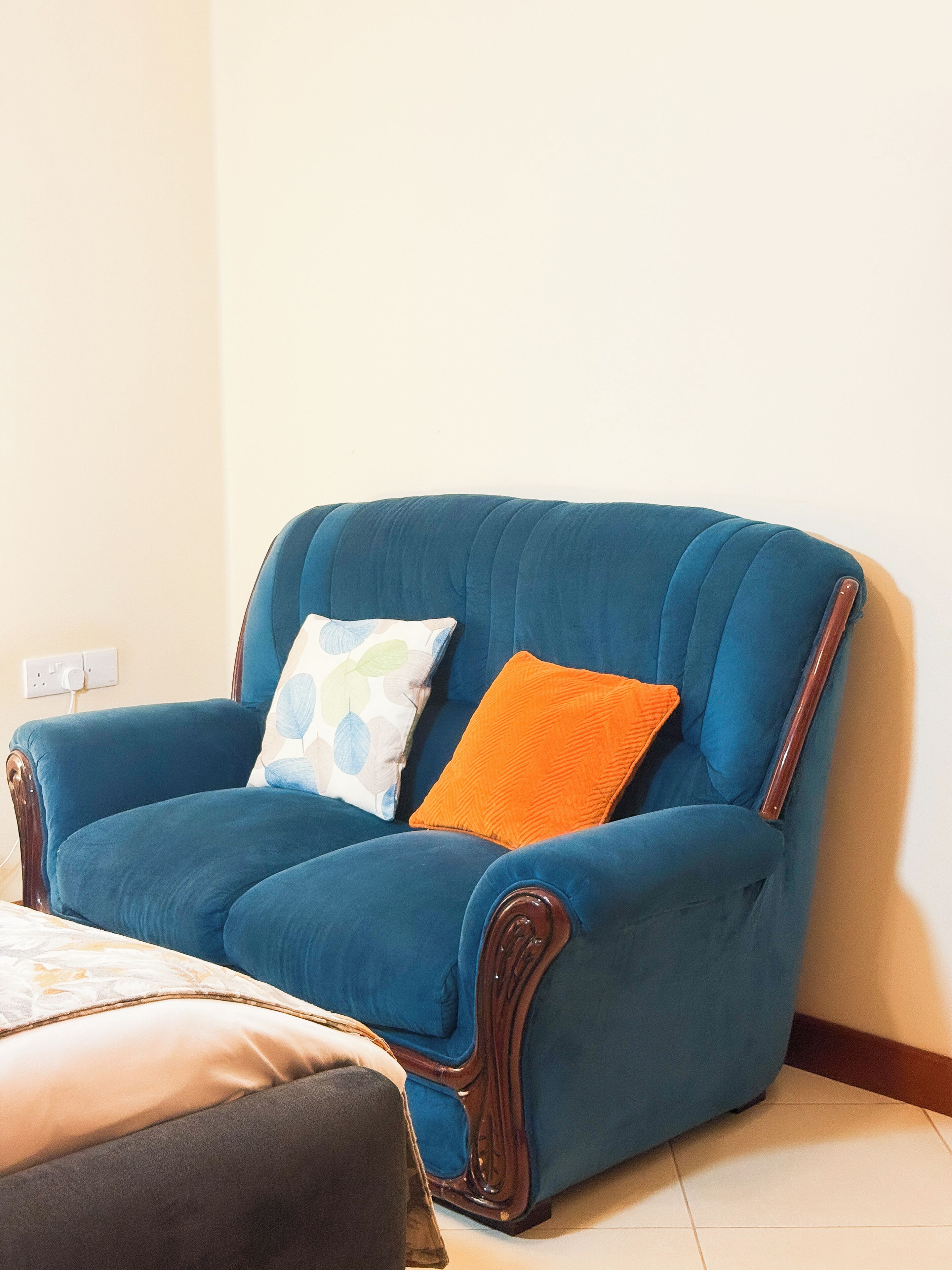 Un sillón azul con dos almohadones, uno blanco y otro naranja, en una habitación con pared blanca y suelo de madera.