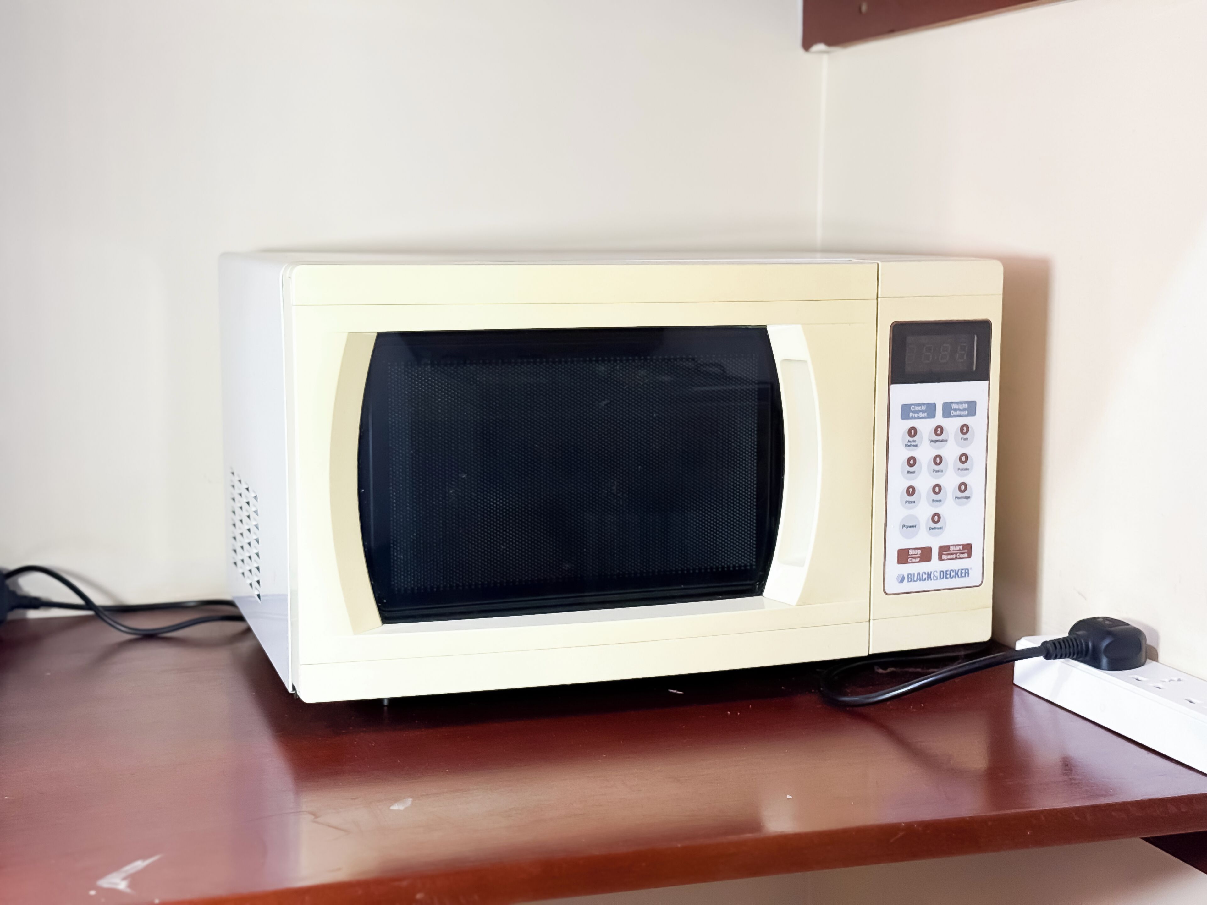 A microwave on a wooden surface with a control panel, a power cord, and a wall socket.