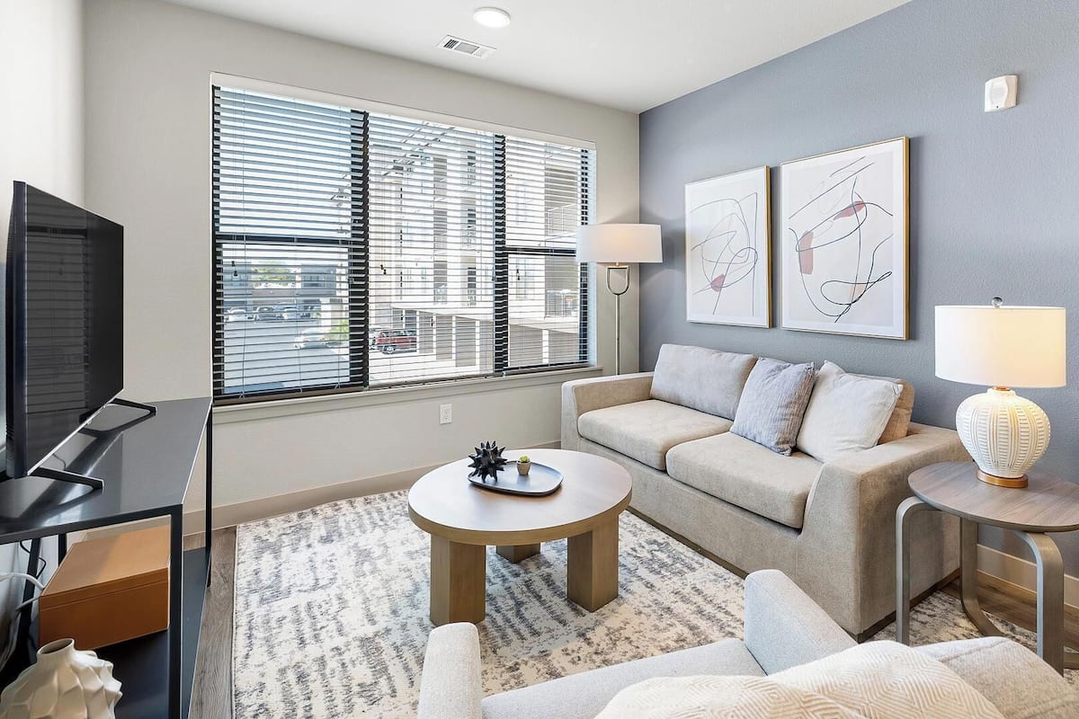 A modern living room with a sofa, coffee table, and TV. There are two lamps and artwork on the wall.