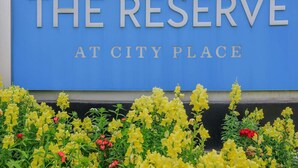 Une enseigne avec l’inscription «
THE RESERVE AT CITY PLACE
» en lettres majuscules, entourée de fleurs jaunes et rouges.