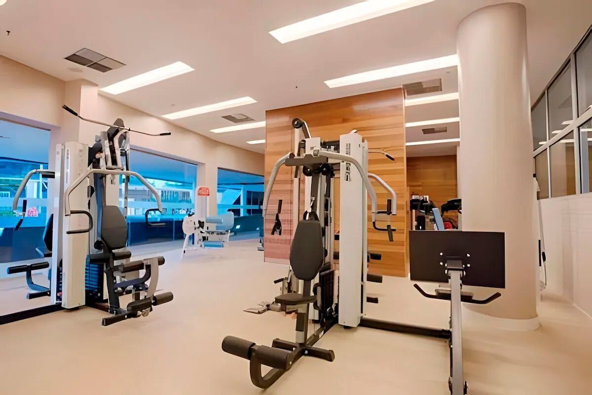 Uma academia moderna com diversos equipamentos de ginástica, um painel de destaque em madeira e janelas amplas.