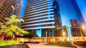 Un immeuble moderne de grande hauteur, doté d’une façade en verre réfléchissant, entouré de verdure et d’autres bâtiments.