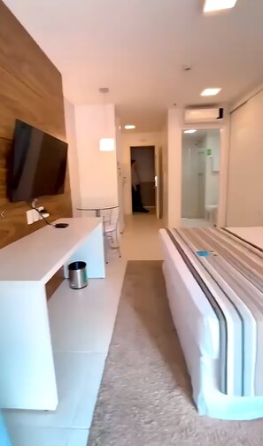 Een moderne hotelkamer met een flatscreen televisie aan de muur, een witte nachtkastje, een ingebouwde bank en een grote spiegel.