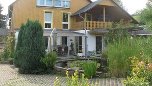 A two-story house with a balcony, a covered patio, and a garden with a pond.