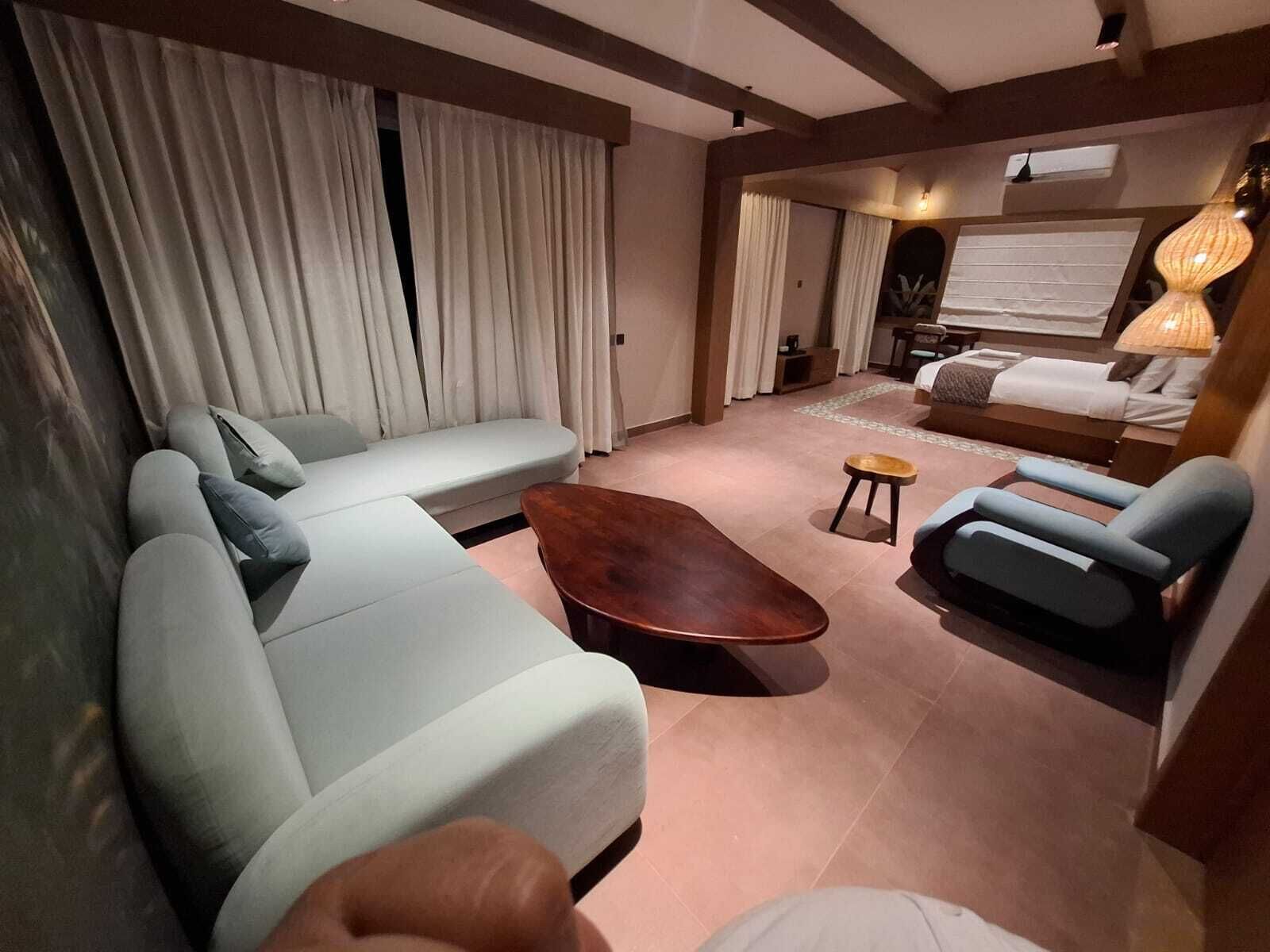 Ein modernes Wohnzimmer mit einer Couch, Sesseln, einem Couchtisch und einem Bett mit einer Lampe.