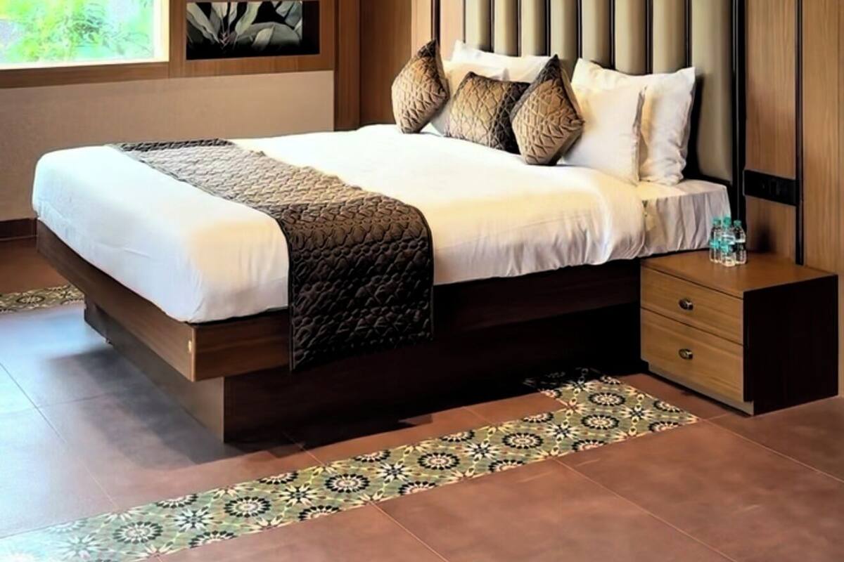 A modern bedroom with a large bed, a ceiling fan, pendant lights, a window with a view, and a decorative wall panel.