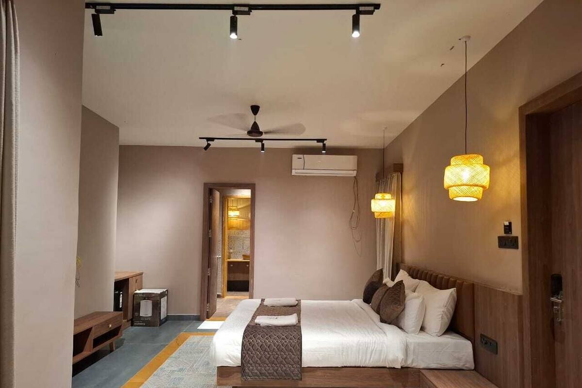 A bedroom with a bed, bedside tables, a ceiling fan, an air conditioning unit, and a hanging light fixture.